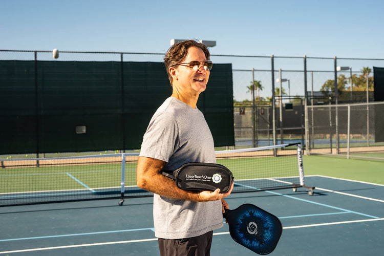 Photo of a man in sunglasses standing on a pickleball court holding a LaserTouchOne device