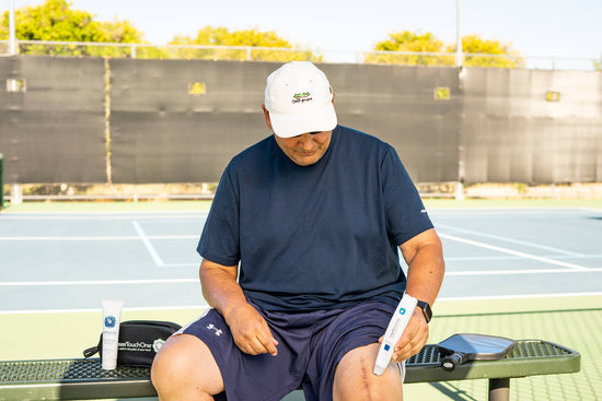 Photo of a man sitting on a bench using a Laser Touch One cold laser therapy device on his knee